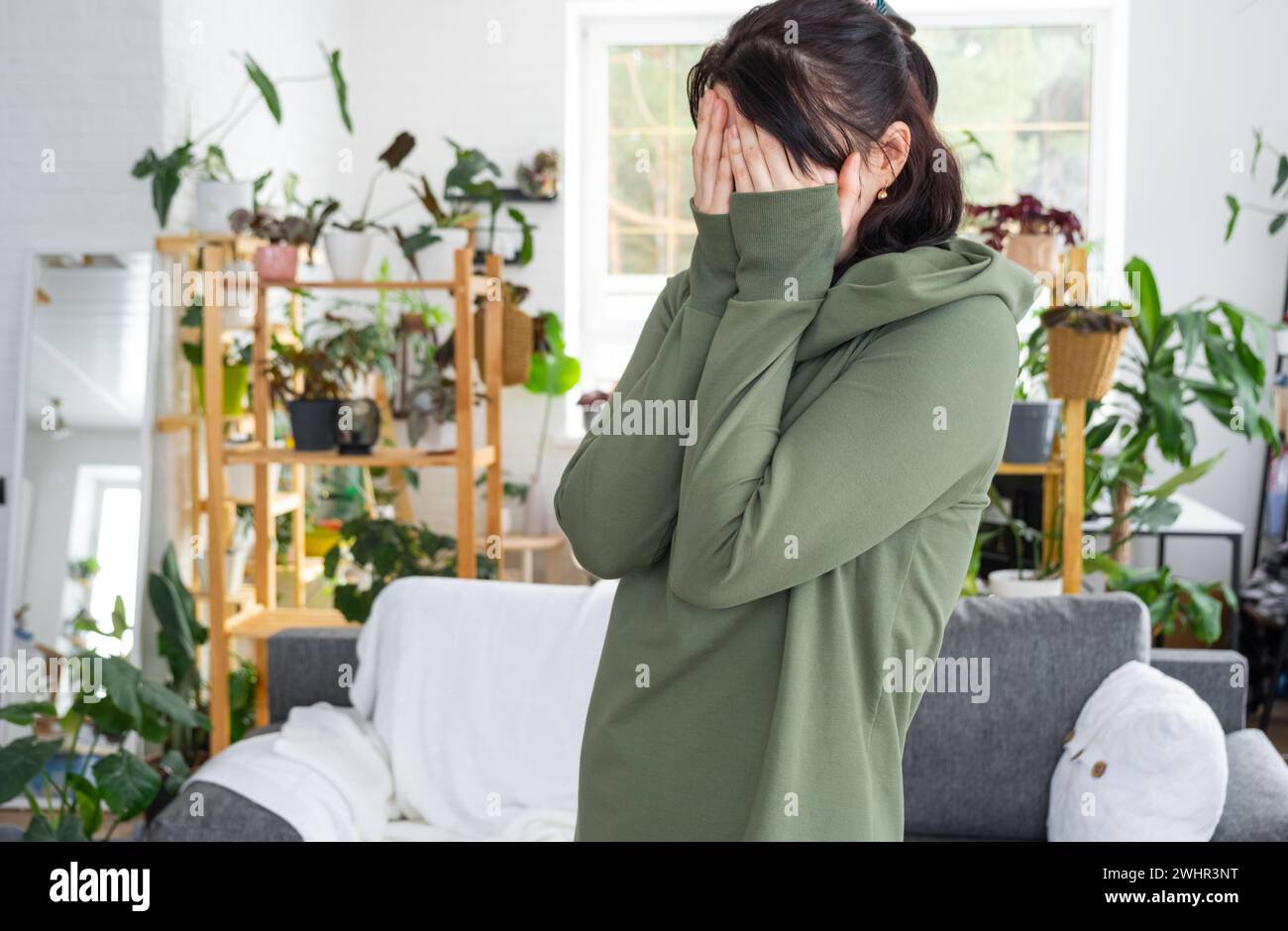 Emozioni affannose e premurose di una donna nella sua casa in un ambiente luminoso e moderno con piante per la casa. Ritratto di un turbamento e. Foto Stock