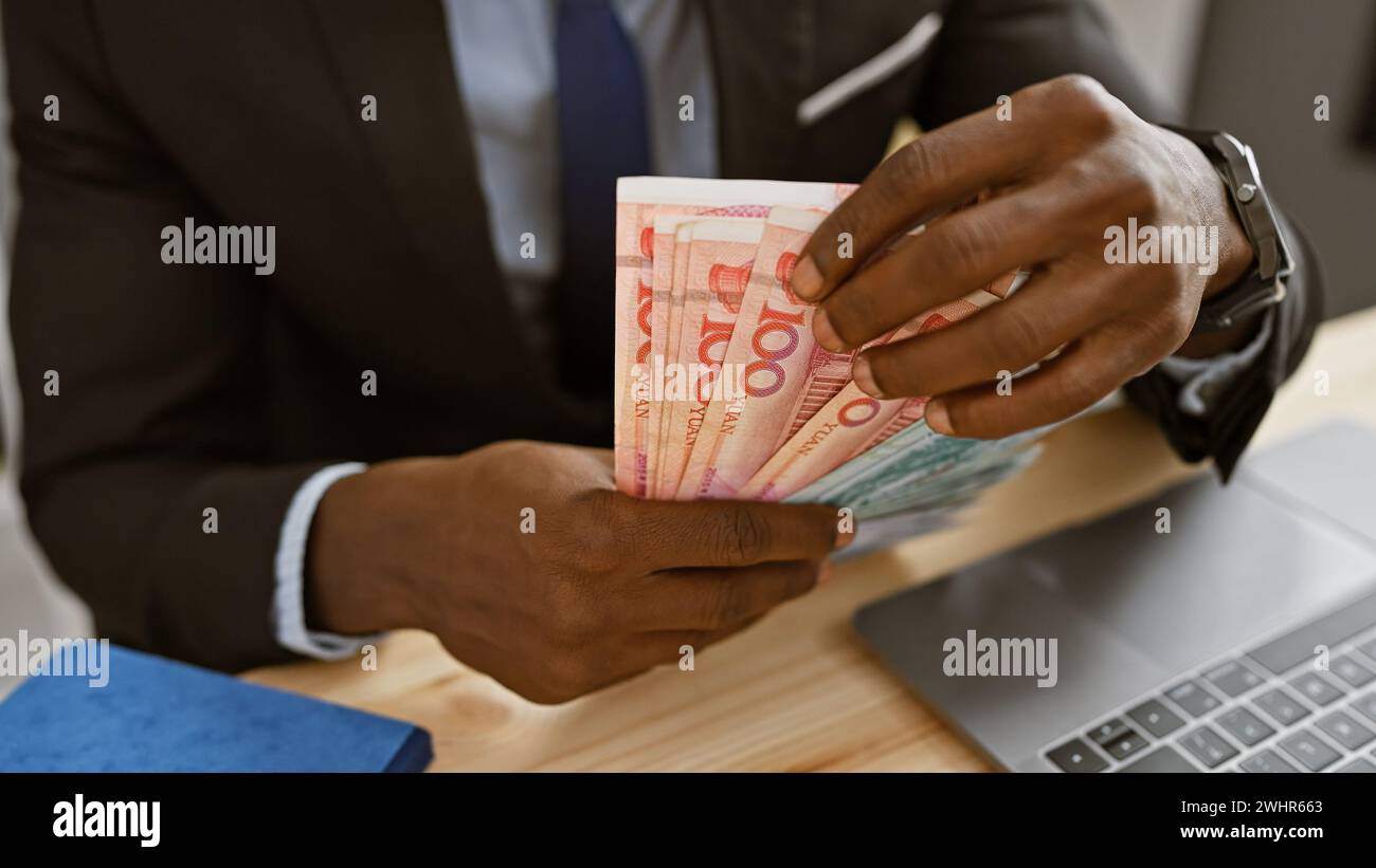 L'uomo africano in ufficio conta lo yuan cinese con notebook e notebook sullo sfondo Foto Stock