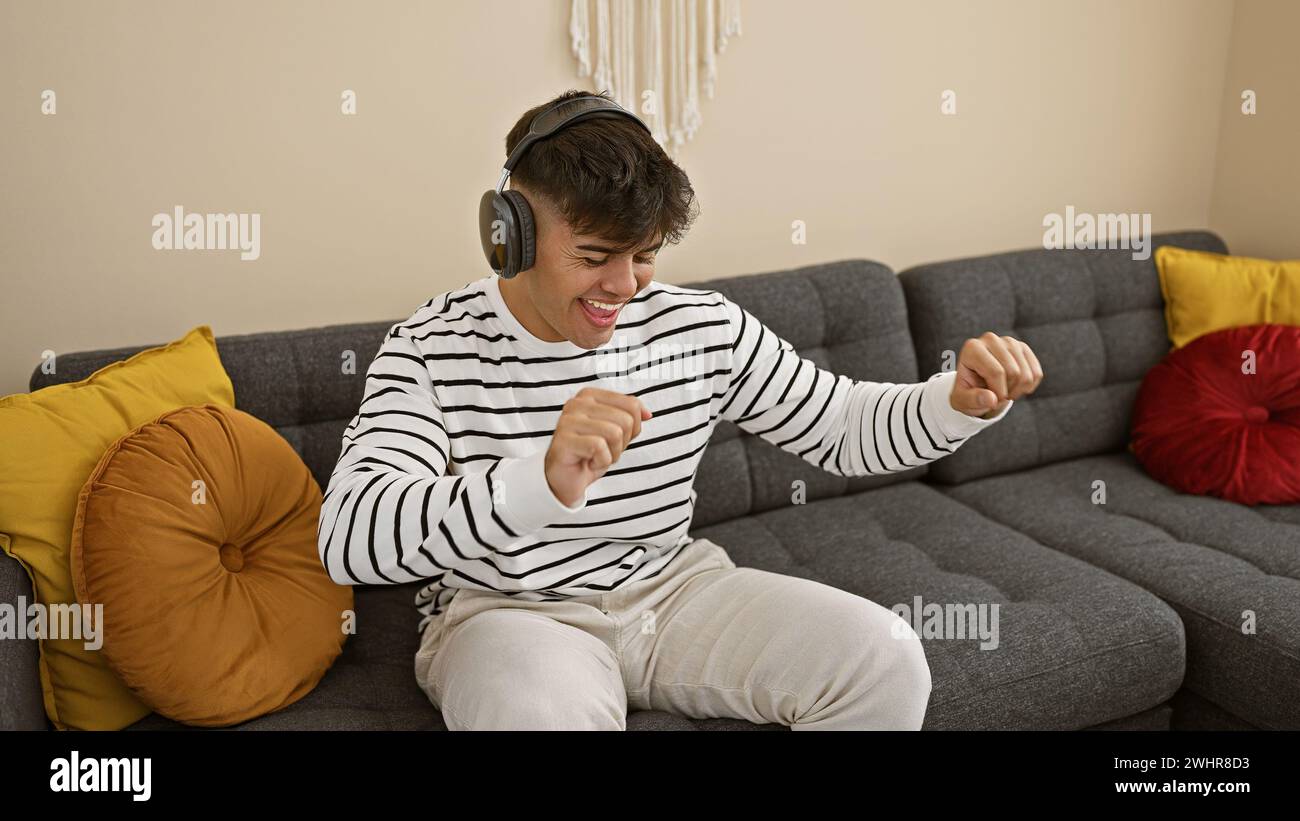 Giovane ispanico seduto sul divano ascoltando musica che ballava a casa Foto Stock