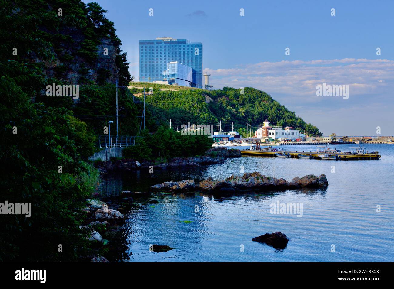 Gangneung City, Corea del Sud - 29 luglio 2019: Le aspre rocce costiere presso il porto di Geumjin, con il maestoso Tops 10 Hotel & Resort arroccato sulle colline Foto Stock