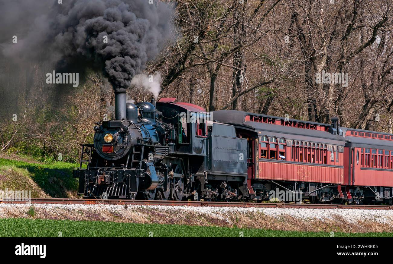 Vista ad angolo di un treno passeggeri a vapore restaurato che si muove lentamente soffiando molto fumo nero Foto Stock