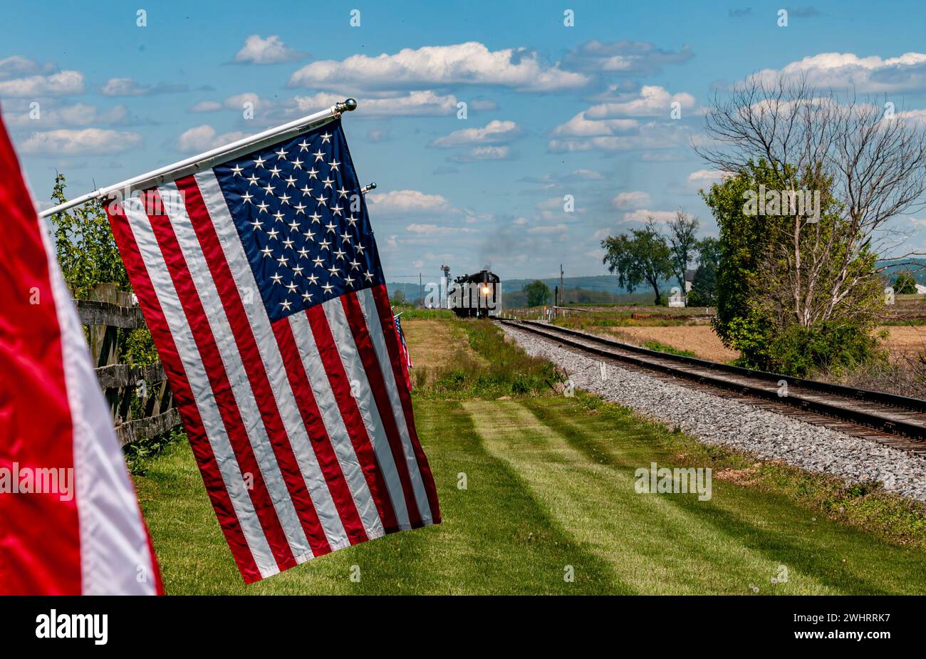 Vista di un motore a vapore in avvicinamento, fumo soffiato e bandiere americane Row che soffrono dolcemente nel vento Foto Stock Vista di un motore a vapore in avvicinamento, fumo soffiato e bandiere americane Row che soffrono dolcemente nel vento Foto Stock