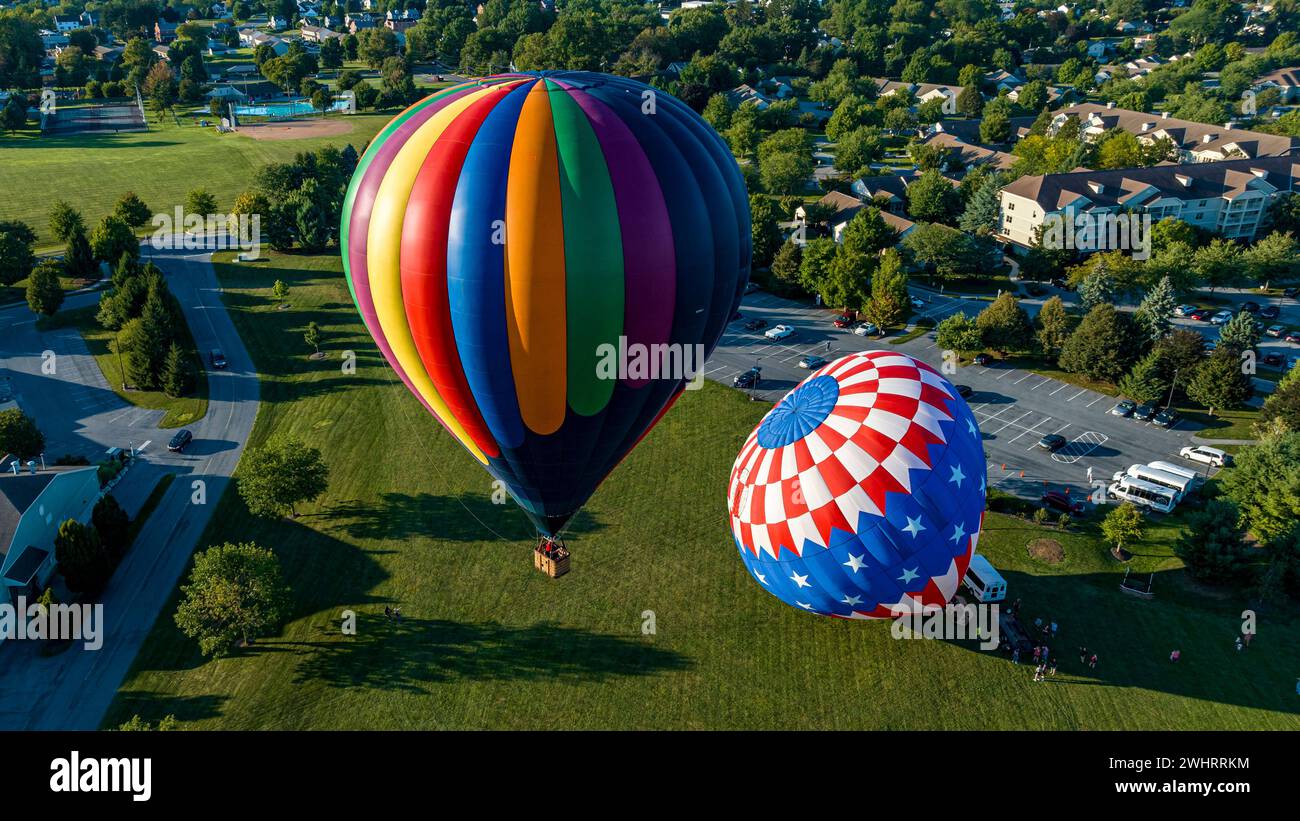 Veduta aerea di una mongolfiera che si prepara per il lancio con una in volo, su un campo in una comunità Foto Stock