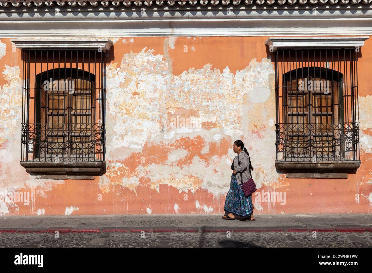 Antigua, Guatemala. Donna che passa accanto a una vecchia casa con vernice sfaldante. Foto Stock