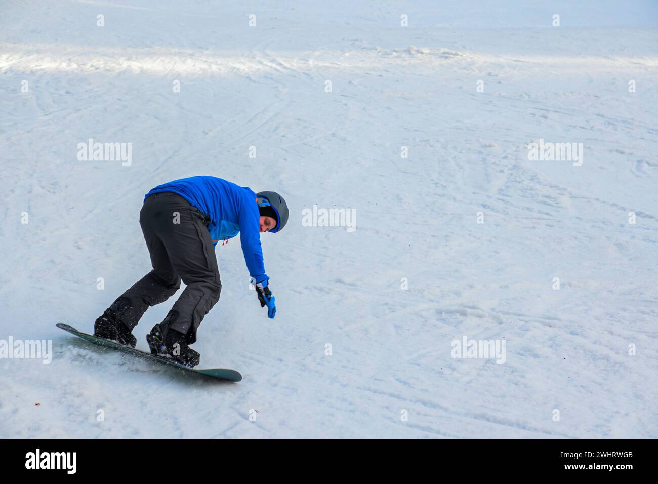 uno snowboarder con una felpa blu e un casco cavalcano su una pista innevata. Foto Stock