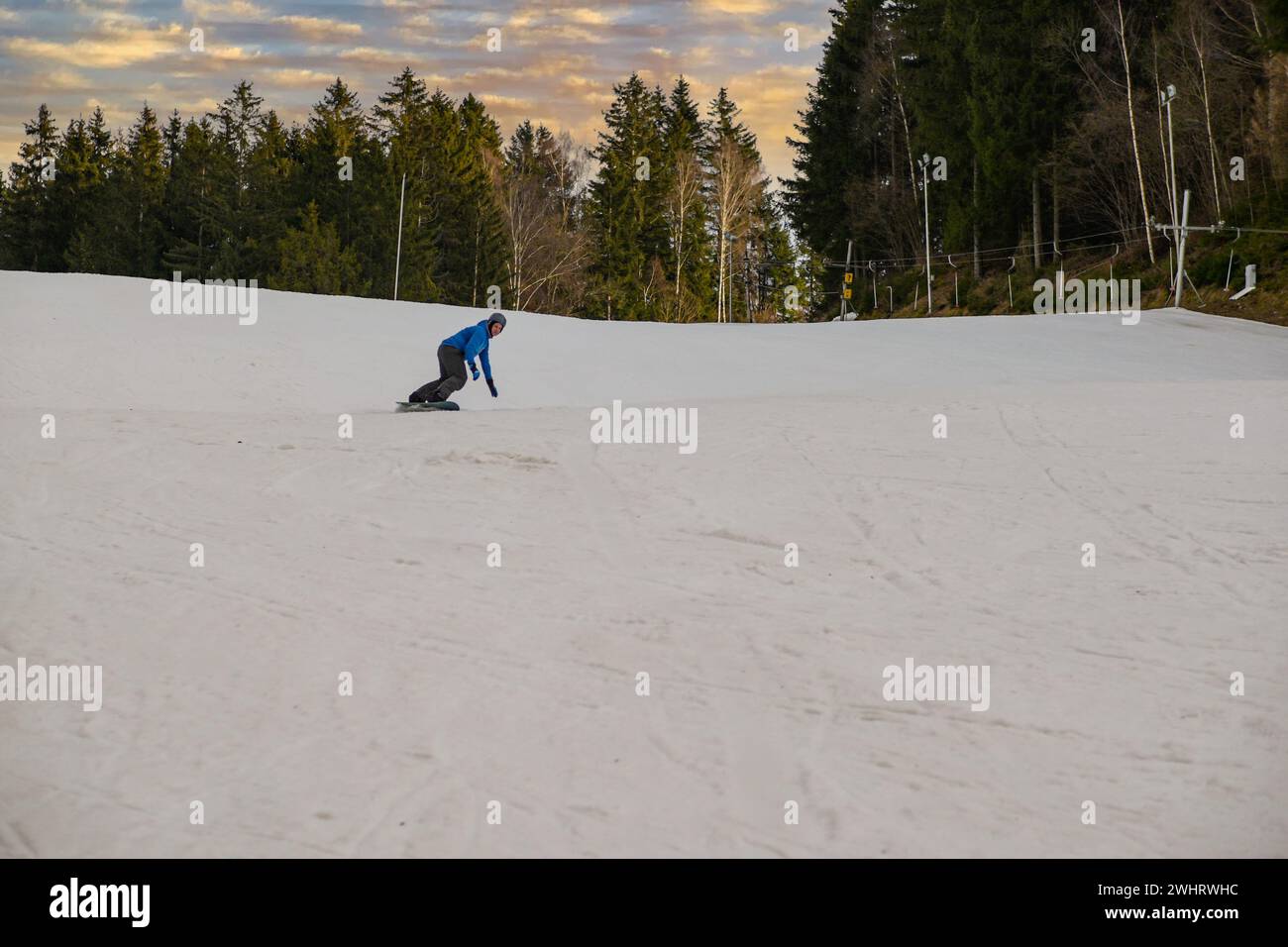 uno snowboarder con una felpa blu e un casco cavalcano su una pista innevata. Foto Stock