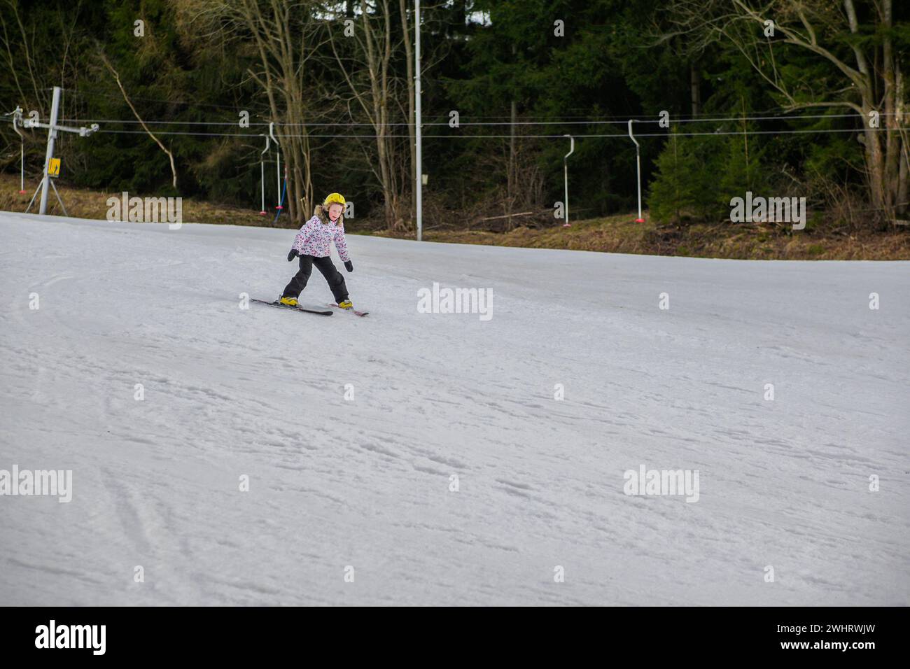 una bambina con un casco giallo sta imparando a sciare. Foto Stock