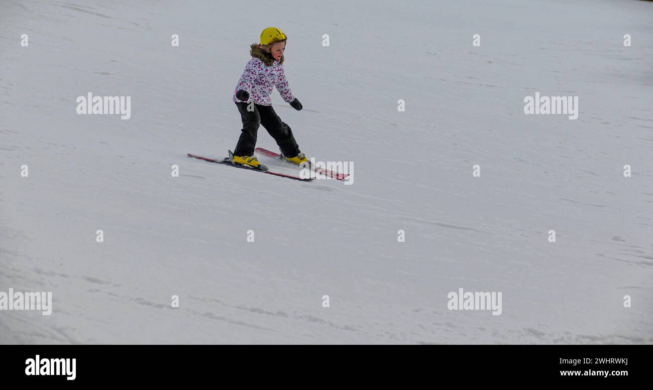 una bambina con un casco giallo sta imparando a sciare. Foto Stock