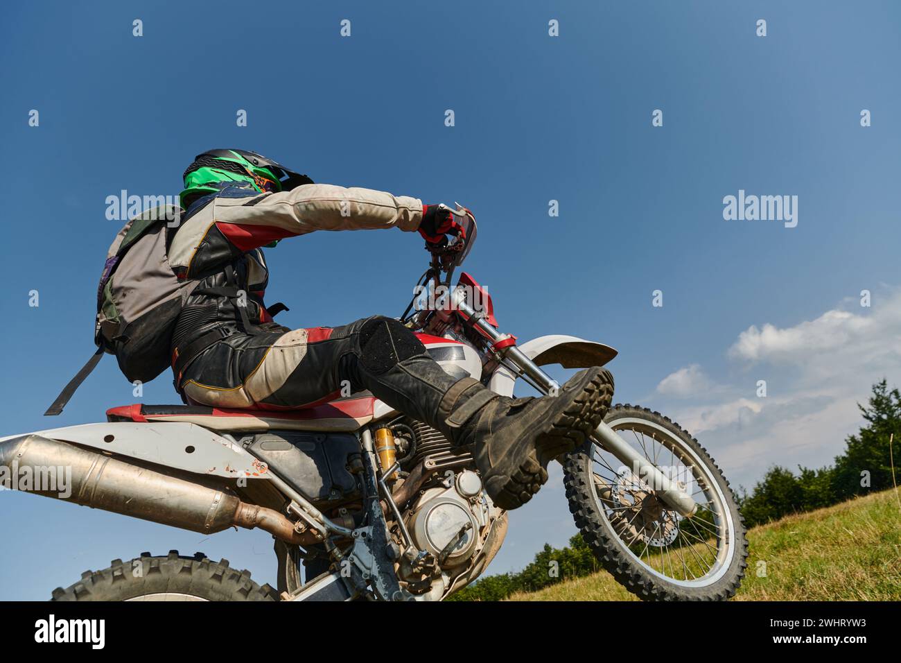 Un intrepido pilota professionista di motocross esegue con abilità una manovra estrema sulla schiena attraverso un pericoloso terreno boschivo, Foto Stock