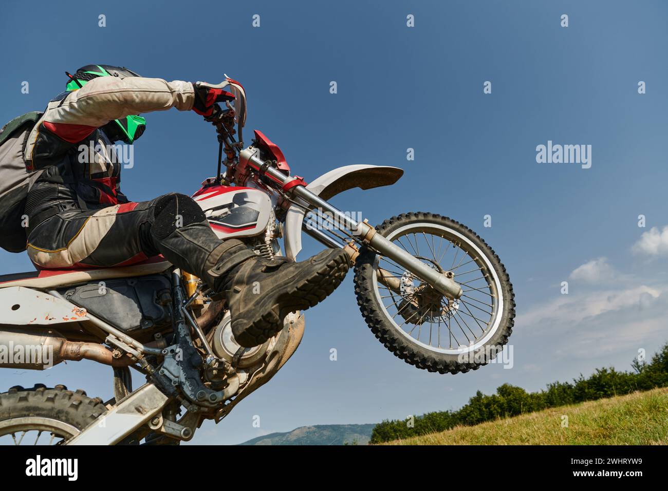 Un intrepido pilota professionista di motocross esegue con abilità una manovra estrema sulla schiena attraverso un pericoloso terreno boschivo, Foto Stock