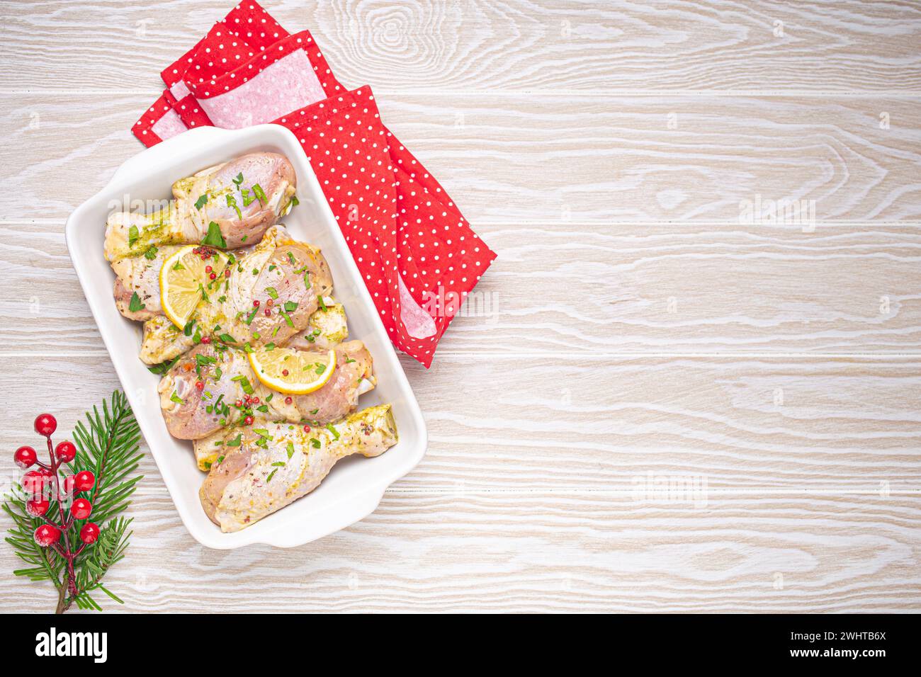 Preparazione del pasto della vigilia di Natale con bacchette di pollo marinate. Cosce di pollo crude con erbe, limone in casseruola bianca a. Foto Stock