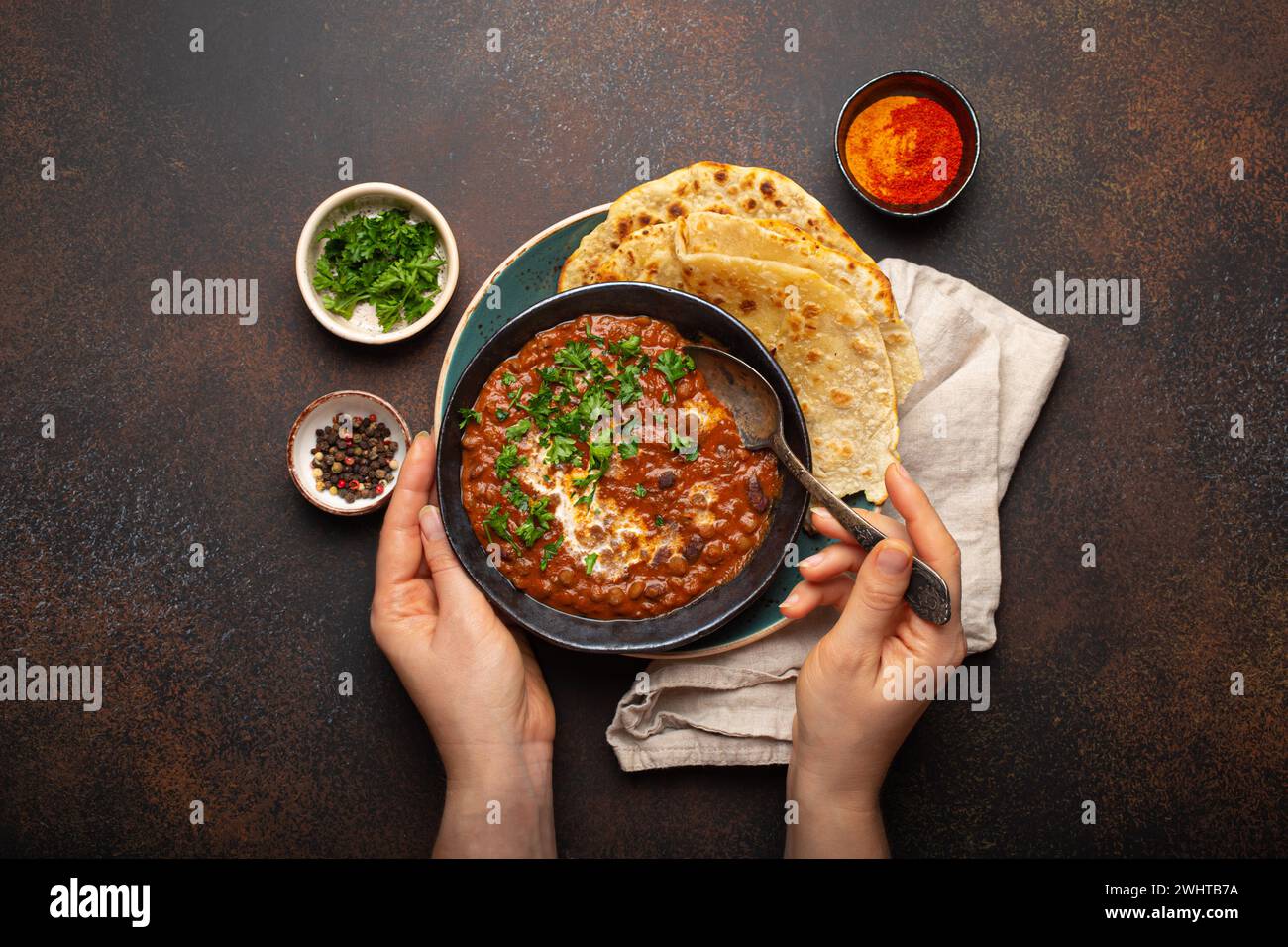 Mani femminili che tengono una ciotola e mangiano il tradizionale piatto Punjabi indiano dal makhani con lenticchie e fagioli serviti con naan flat Foto Stock