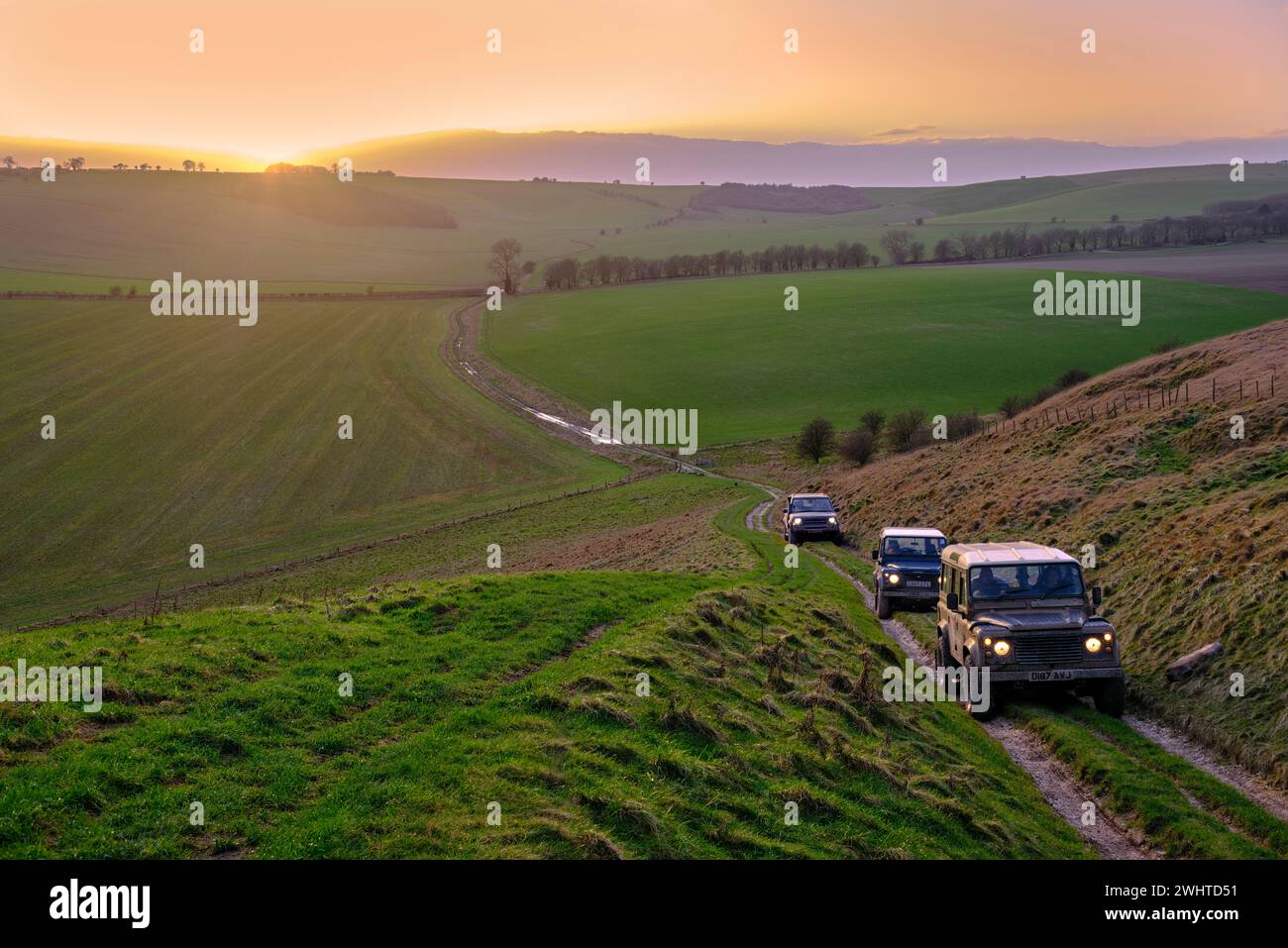 Land Rovers sale su una strada per Sugar Hill sul Marlborough Downs al tramonto. Wiltshire, Inghilterra. Foto Stock