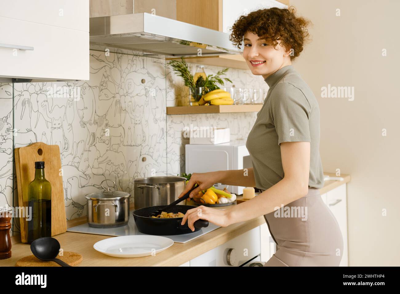 Una donna sorridente mette su un piatto la pasta cotta con salsa di funghi da una padella Foto Stock