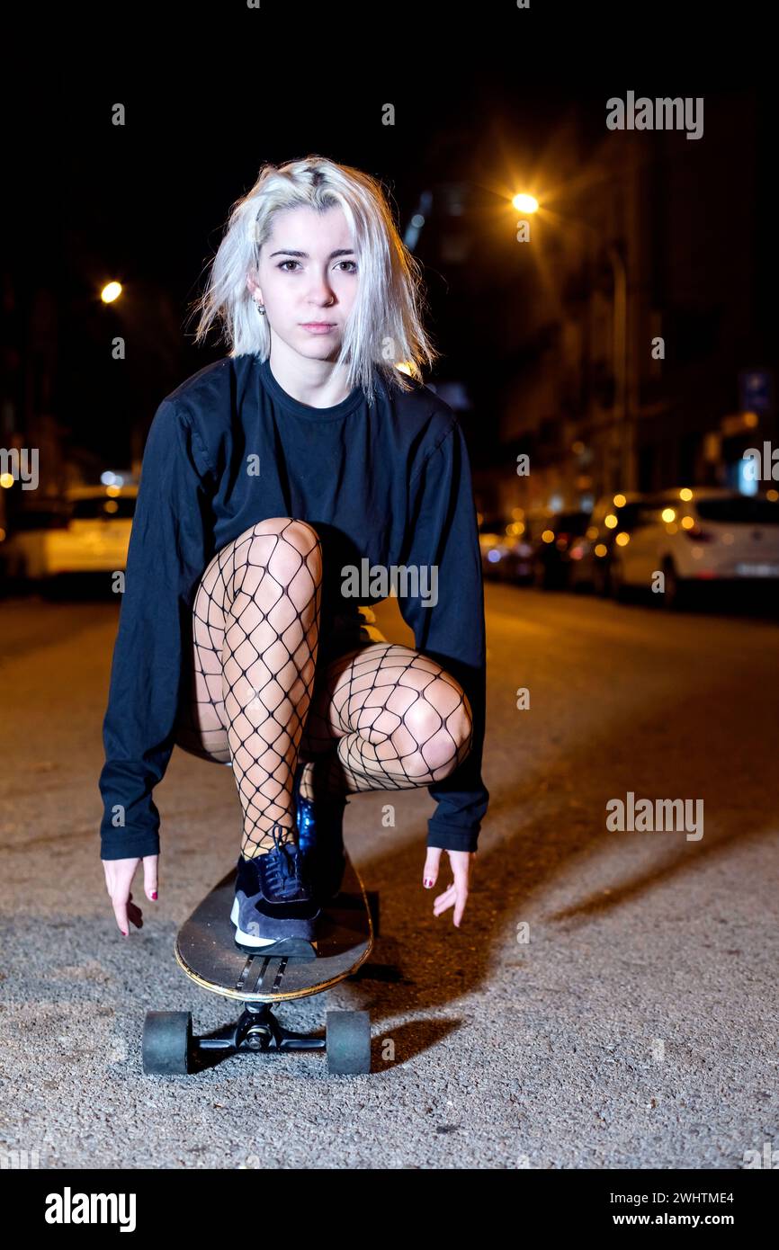 Giovane donna in shorts da surf mentre guarda la macchina fotografica di notte in città Foto Stock