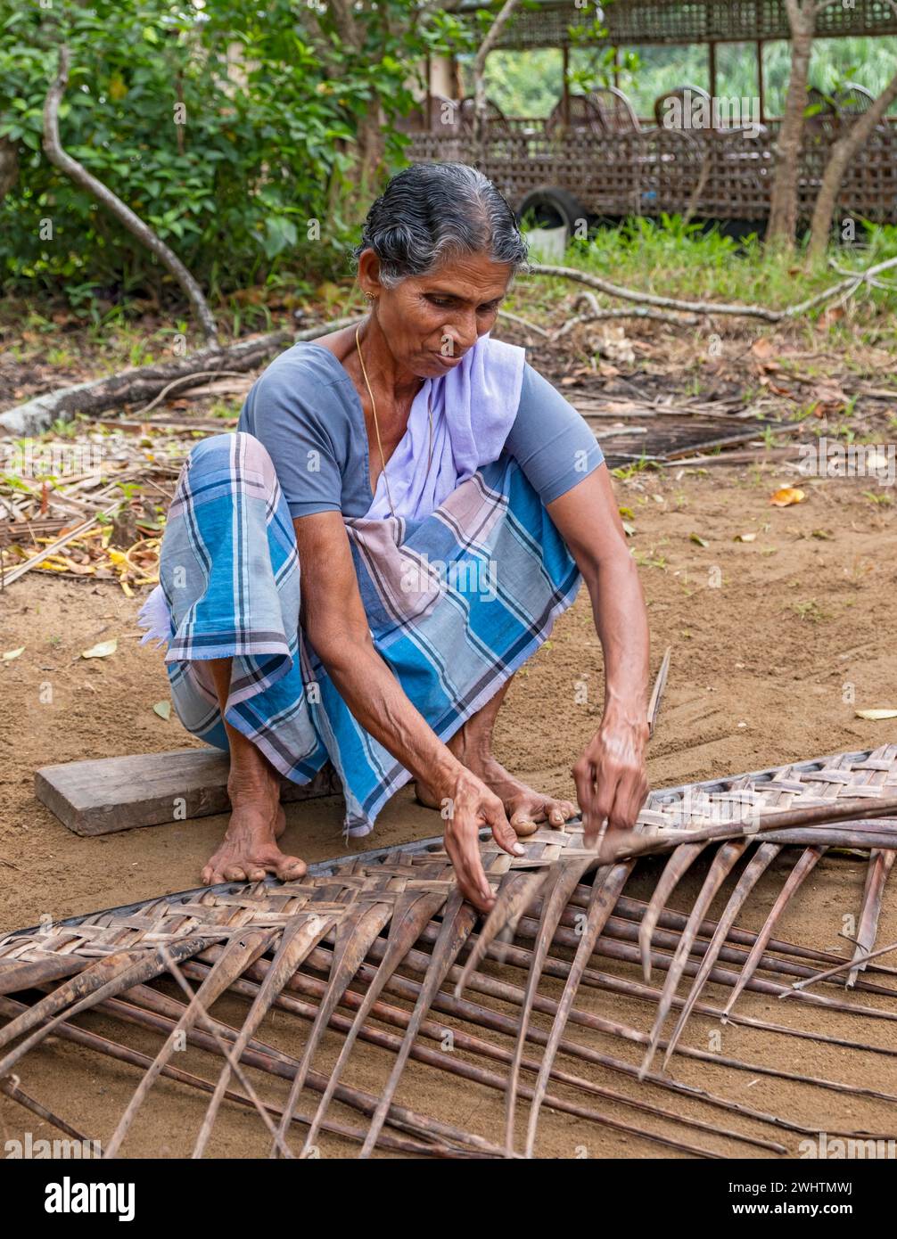 Una donna del villaggio dimostra il tradizionale mestiere di realizzare tappeti da foglie di cocco usando le dita dei piedi, Kerala Backwaters, Kerala, India Foto Stock