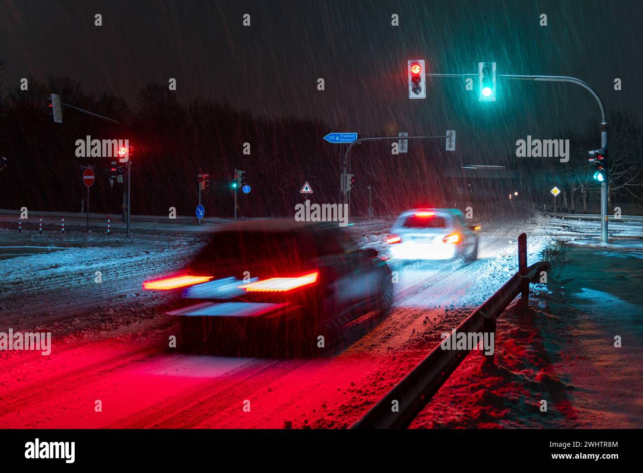 Auto che guidano lungo una strada di notte, passando sotto un segnale stradale Foto Stock