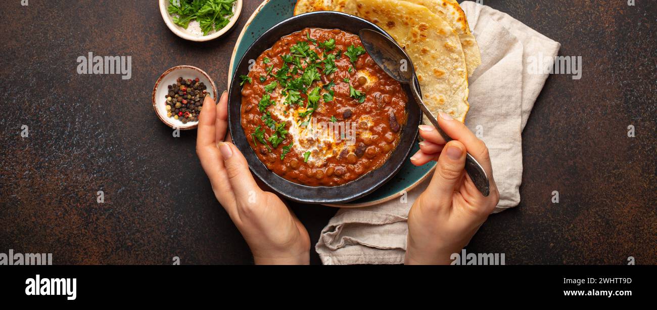 Mani femminili che tengono una ciotola e mangiano il tradizionale piatto Punjabi indiano dal makhani con lenticchie e fagioli serviti con naan flat Foto Stock