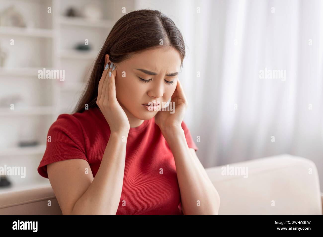 Giovane donna asiatica in difficoltà che tiene le orecchie e soffre di dolore Foto Stock