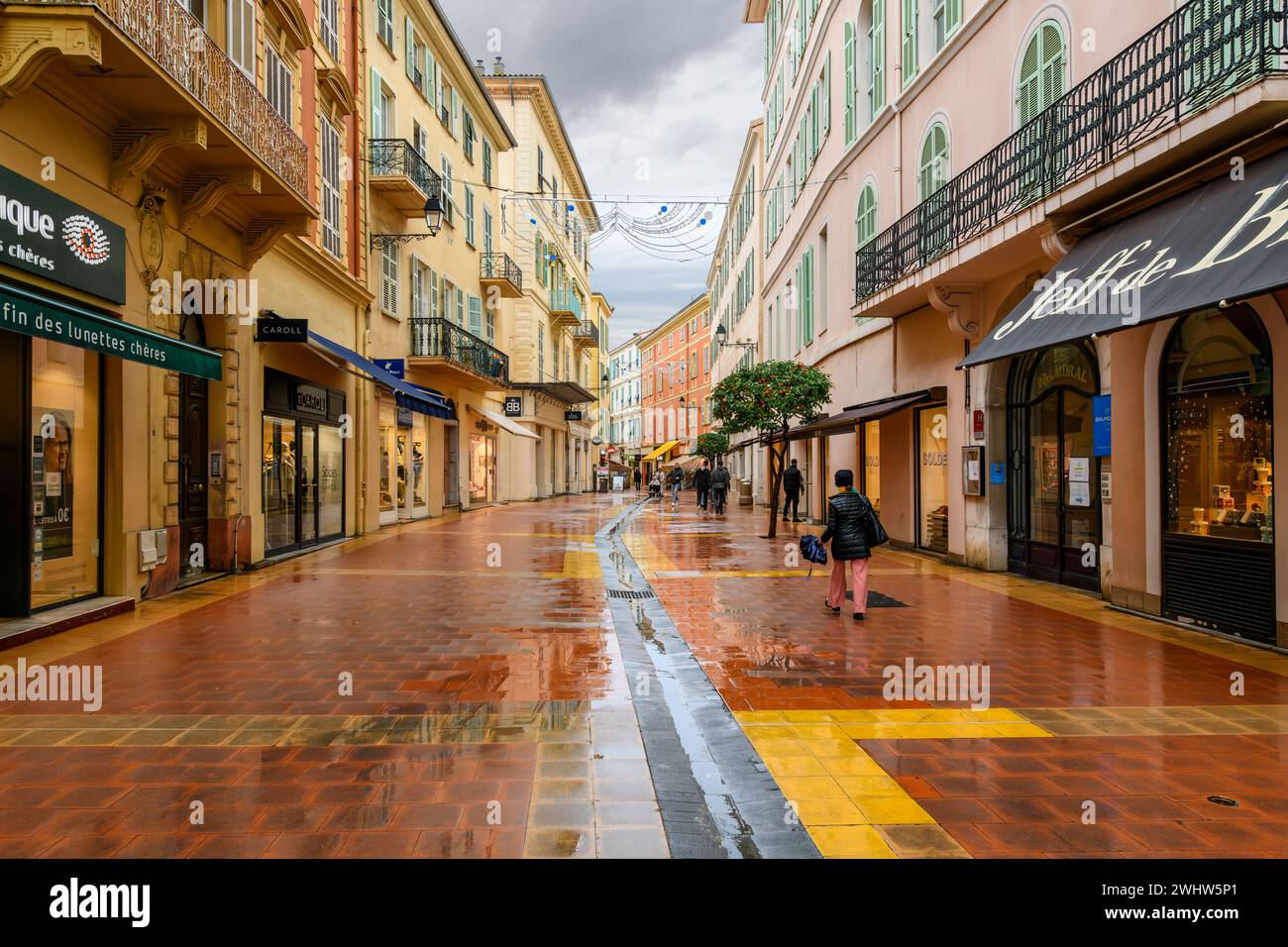 Una mattinata piovosa mentre i pedoni camminano per le strade bagnate passando davanti a negozi e caffetterie nel centro storico di Mentone, in Francia, lungo la Costa Azzurra Foto Stock