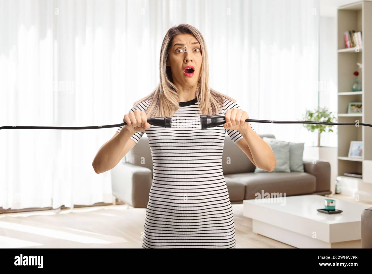 Una giovane donna scossa che tiene i cavi elettrici a casa in salotto Foto Stock