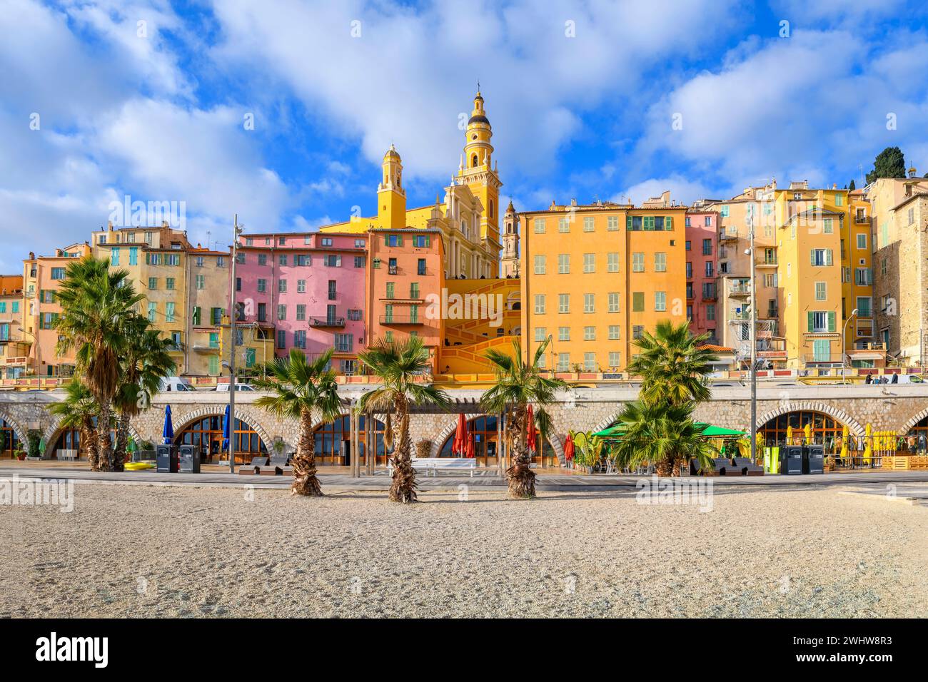Vista dalla spiaggia di Plage des Sablettes e dal lungomare della colorata città vecchia di Mentone in Francia, la cattedrale, il campanile e i gradini della basilica Foto Stock