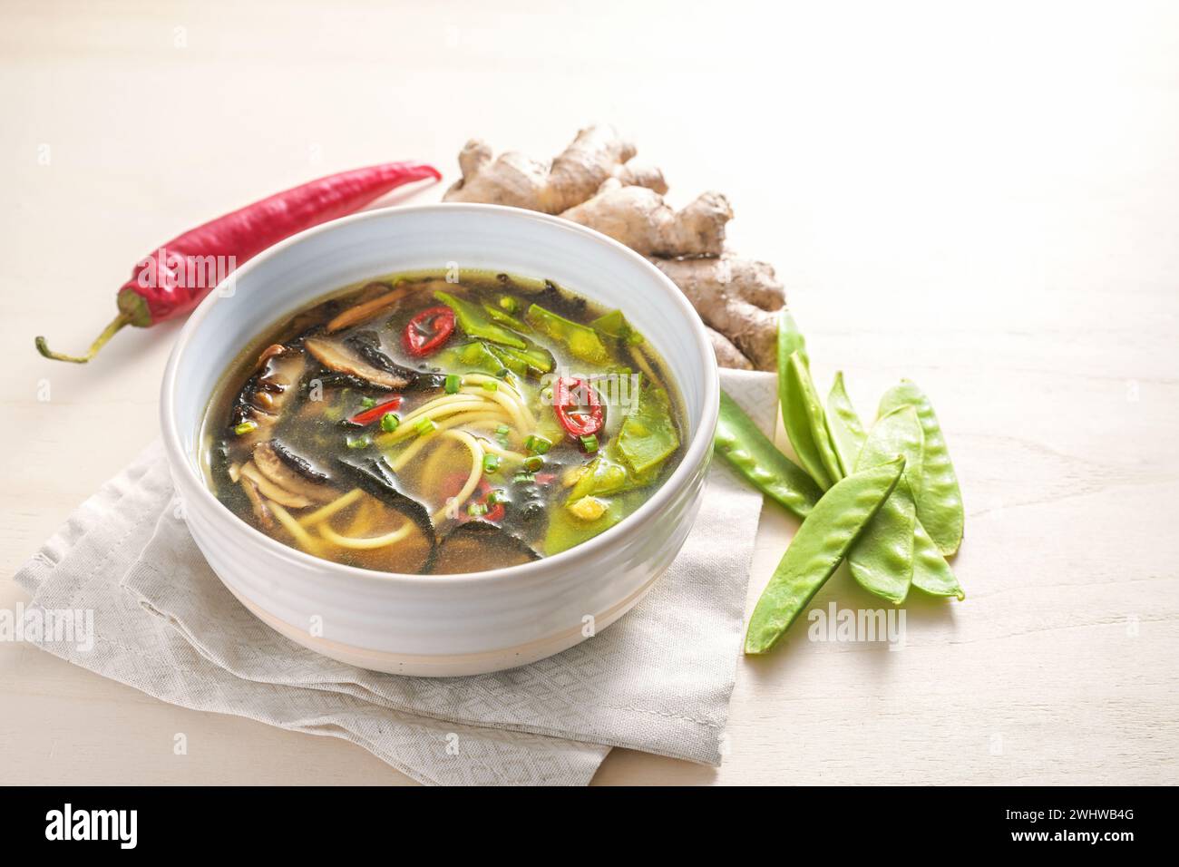 Zuppa piccante di verdure asiatiche con spaghetti, miso, alghe nori, zenzero e peperoncino in una ciotola su un tavolo di legno, copia spazio, selezionato Foto Stock