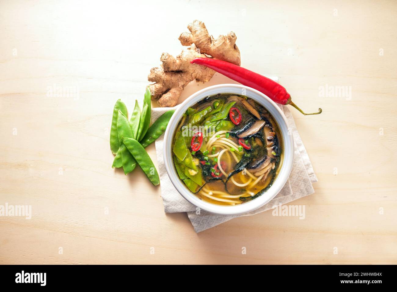 Zuppa vegetariana, cucinata in stile asiatico con verdure, tagliatelle, miso, alghe nori, zenzero e peperoncino in una ciotola su un tavolo di legno Foto Stock