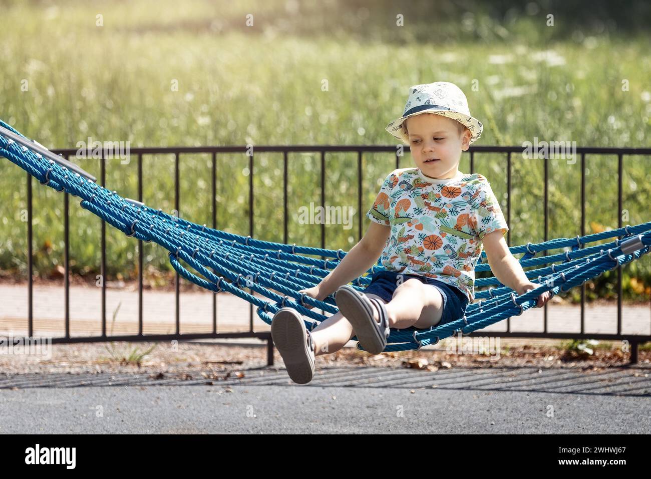 Un bambino da sogno oscilla su un'amaca nel parco durante l'estate. Il concetto di svago e svago per i bambini in città. Foto Stock