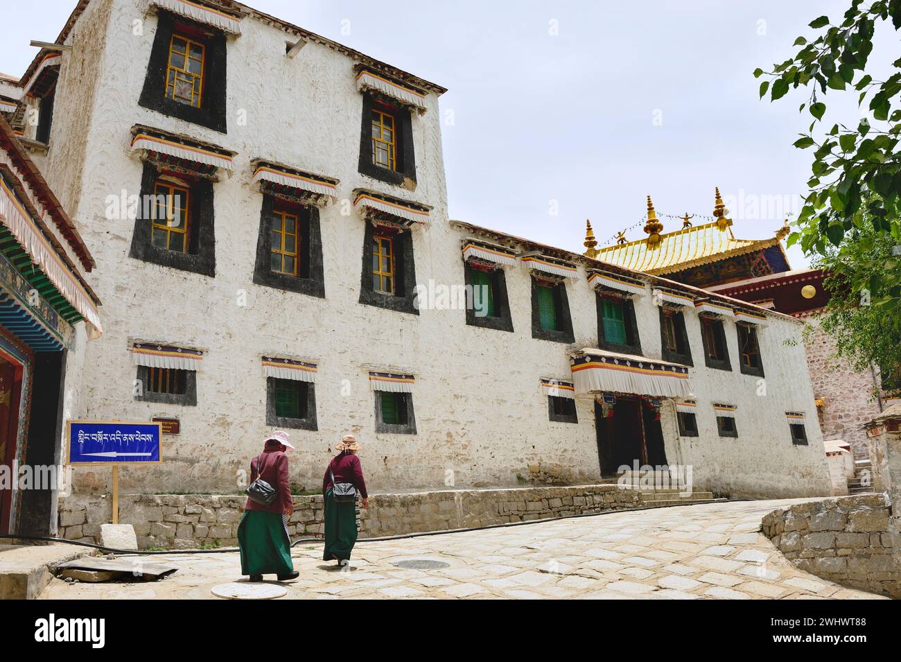 Due donne camminano lungo una strada acciottolata al Monastero di sera, situato appena fuori Lhasa, regione Autonoma Cinese del Tibet. Foto Stock