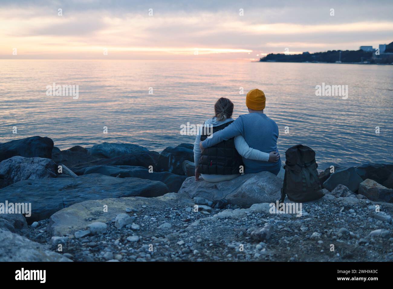 Marito e moglie seduti su enormi pietre vicino all'acqua e tenersi per mano la sera. Foto Stock