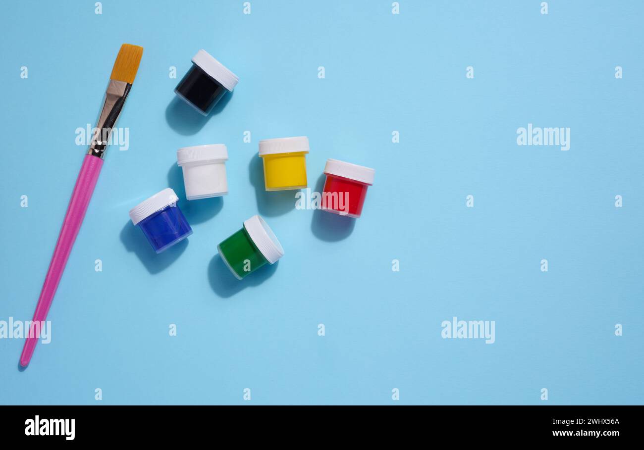 Vasetti di plastica con gouache multicolore su sfondo blu, spazio copia Foto Stock