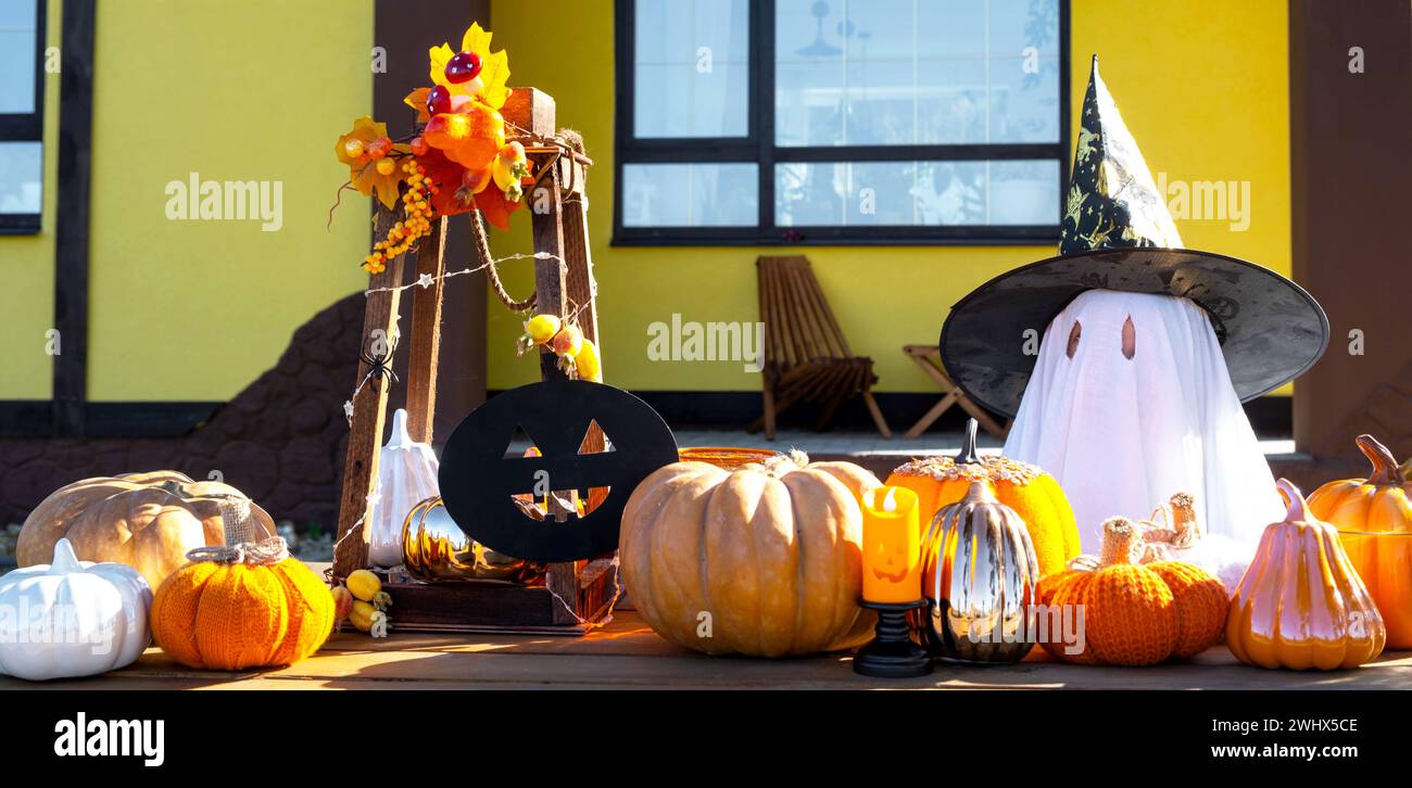 Bambino in lenzuola con fessure come fantasma nel cappello da strega e decorazioni di Halloween sul portico della casa all'esterno nel cortile della puma Foto Stock