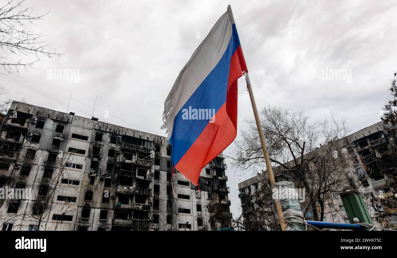 Bandiera tricolore della Russia sullo sfondo di case distrutte e bruciate in Ucraina Foto Stock
