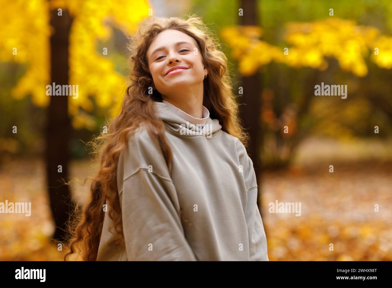 Giovane donna sorridente che si gode il tempo autunnale nella foresta con le foglie gialle al tramonto. Foto Stock