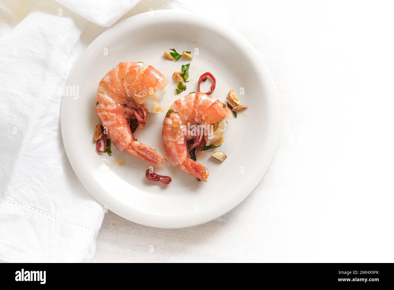 Due gamberetti tigre fritti o gamberetti con peperoncino rosso, aglio ed erbe aromatiche su un piatto bianco, pasto di pesce piccante, vista dall'alto Foto Stock
