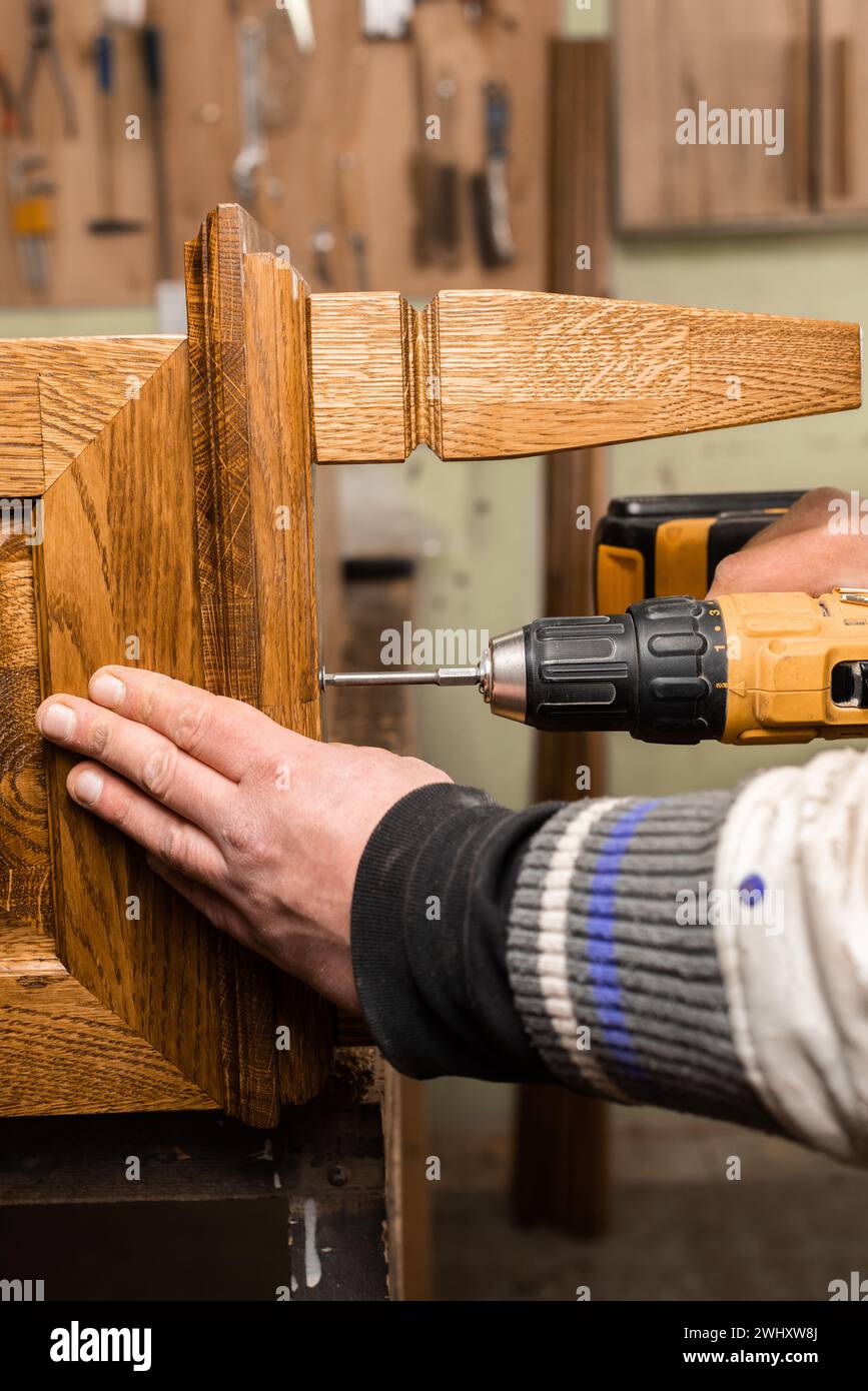 L'uomo fora gli elementi in legno dell'armadio e lo tiene con la mano in verticale Foto Stock
