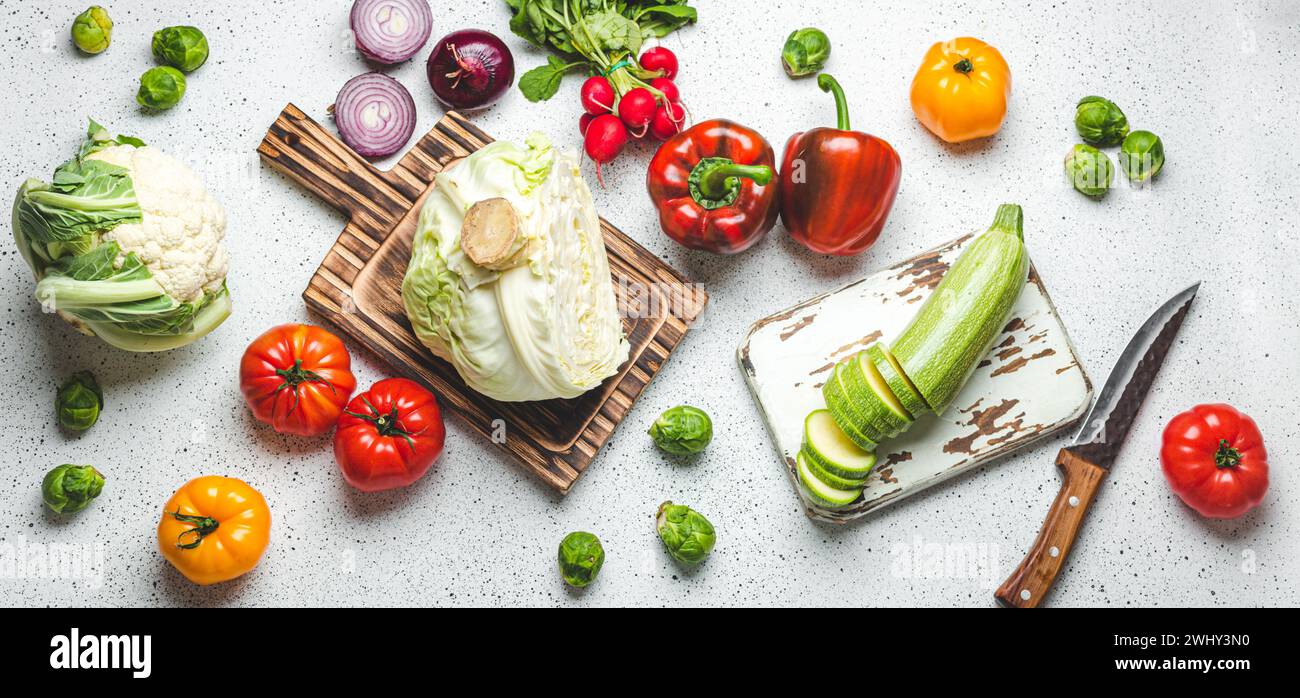 Verdure fresche con taglieri in legno e coltello su tavolo da cucina bianco. Cucina vegetariana da Heal Foto Stock