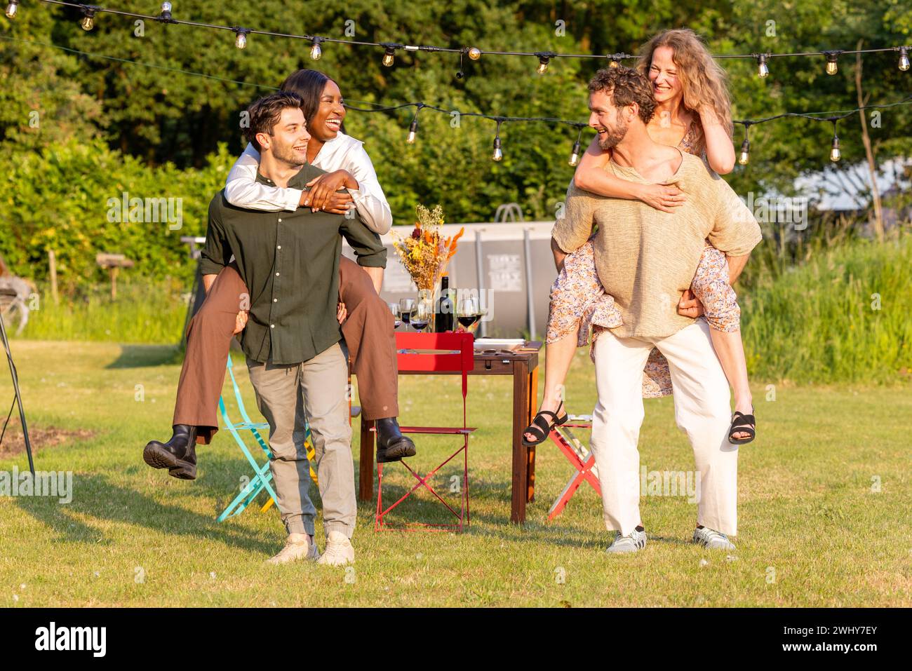 Amici millenari multietnici impegnati in Fun Piggyback Race al Garden Party Foto Stock