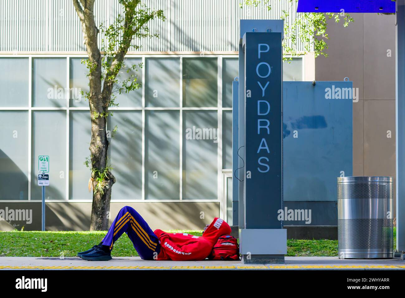 NEW ORLEANS, LOUISIANA, USA - 31 DICEMBRE 2023: Uomo vestito in modo intelligente che indossa un colorato abbigliamento atletico reclinato presso la fermata del tram Poydras su Loyola Ave. Foto Stock