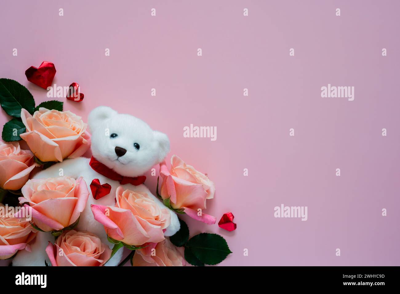 Bambola bianca orsacchiotto con rose rosa e forma d'amore su sfondo rosa per San Valentino. Foto Stock