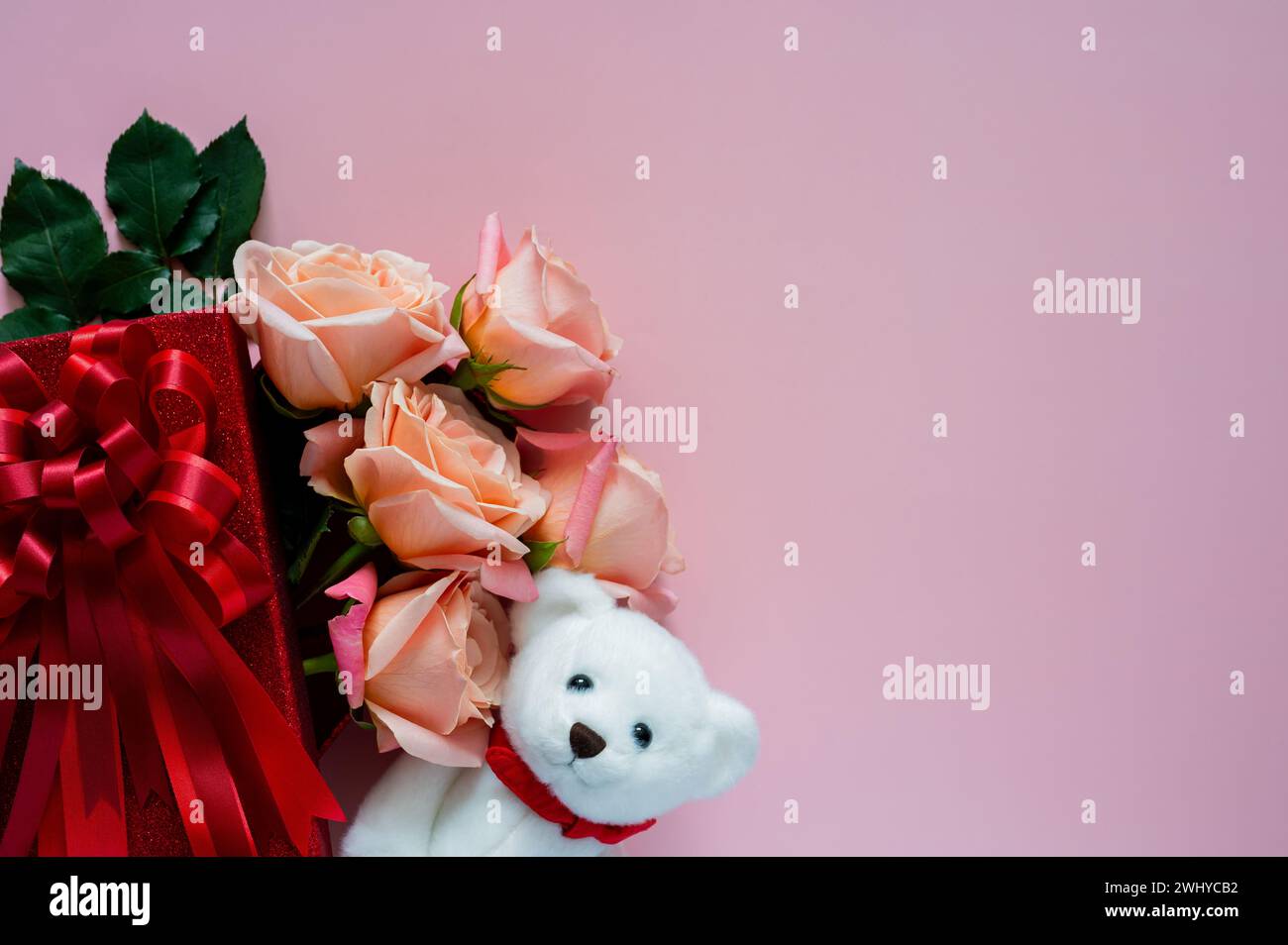Rose rosa in confezione regalo rossa con bambola orsacchiotto bianca su sfondo rosa per San Valentino. Foto Stock