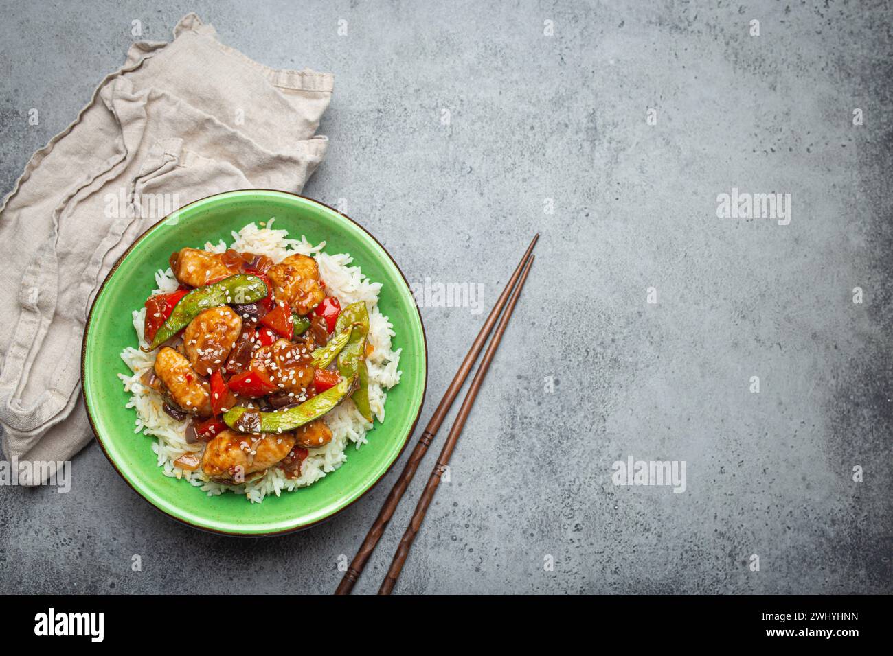 Pollo asiatico agrodolce e appiccicoso con verdure, friggere e riso in un recipiente di ceramica con bacchette, vista dall'alto su rustico grigio st Foto Stock