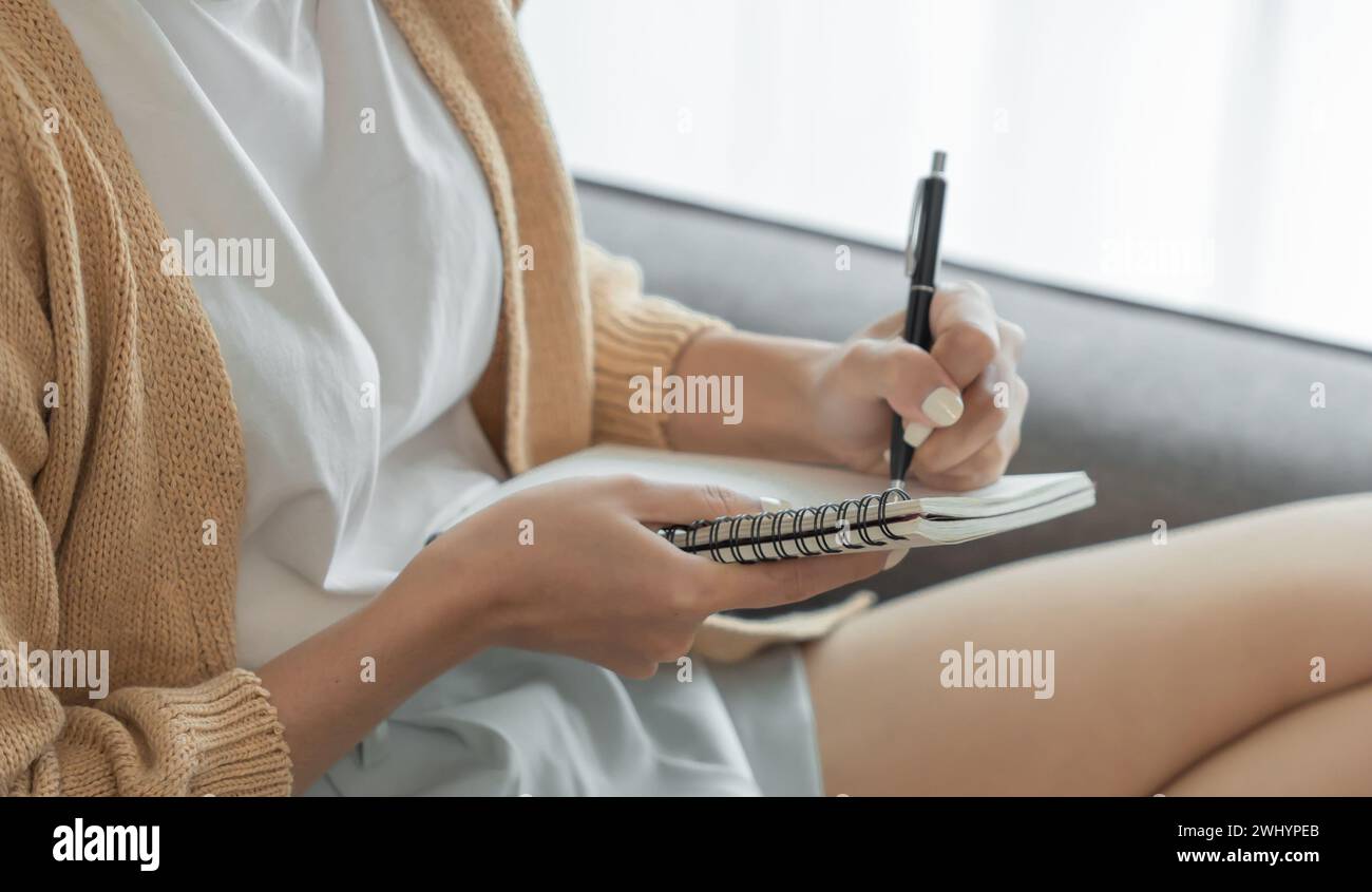 Donna di affari asiatica che lavora dall'ufficio prendendo appunti di lettura e scrittura in blocco note Foto Stock