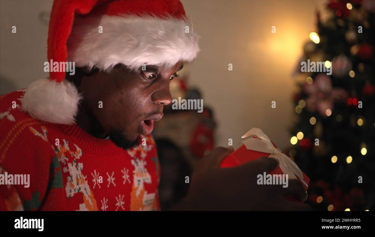 Giovane seduto sulla sedia di fronte all'albero di Natale e aprendo una confezione regalo, buon Natale e buone feste! Foto Stock