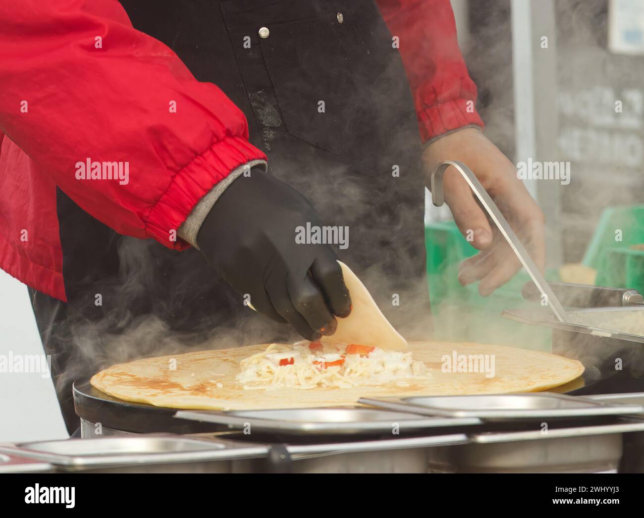 Corpo di un uomo che prepara pancake o crepes francesi con formaggio e prosciutto al mercato del cibo di strada degli agricoltori sul lungomare di Naplavka a Praga, Repubblica Ceca Foto Stock