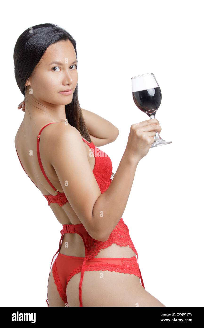 Giovane donna asiatica che indossa lingerie rosse e regge un bicchiere di vino rosso isolato su uno sfondo bianco con spazio per le copie Foto Stock