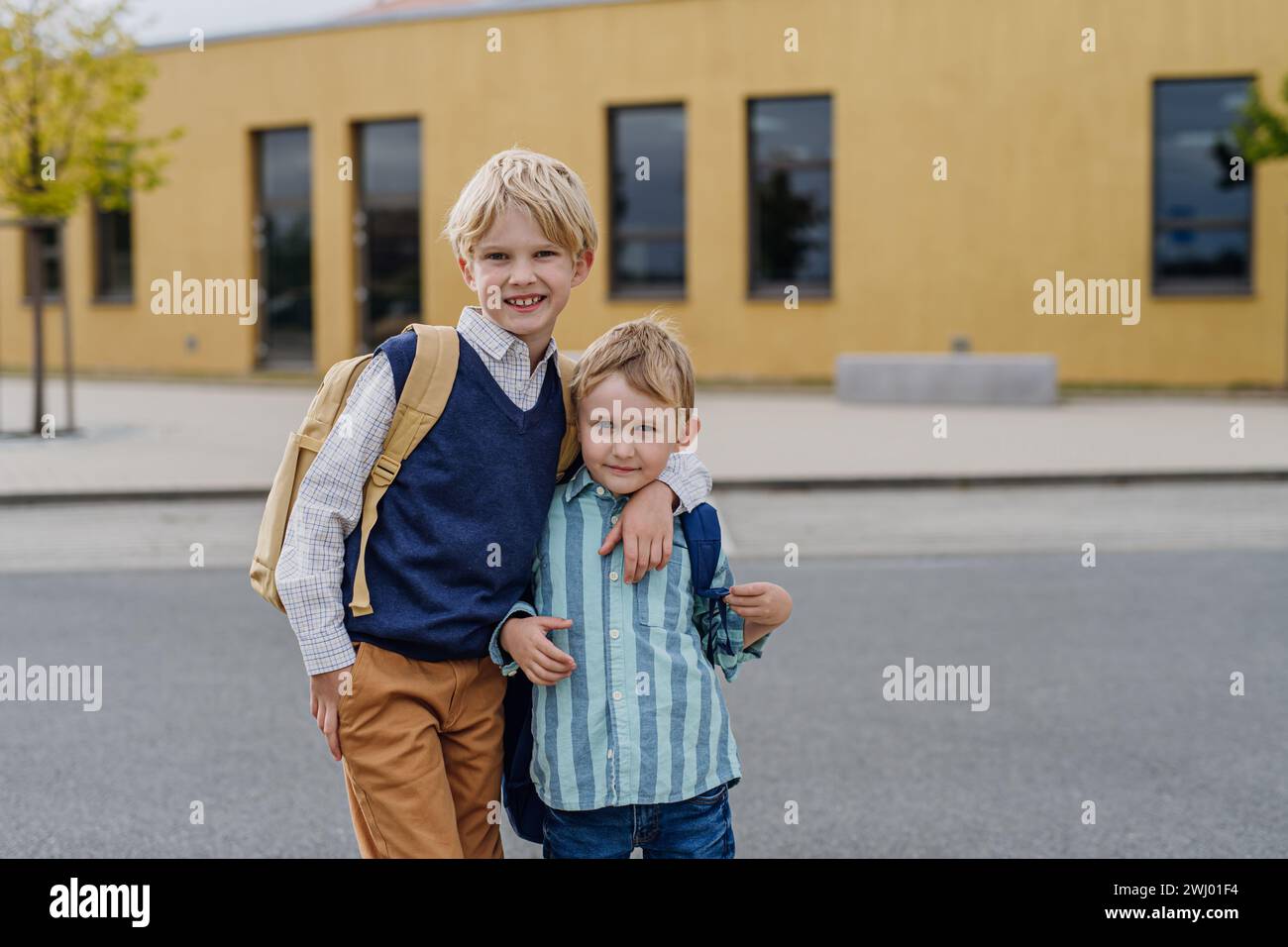 Ritratto di due fratelli davanti all'edificio scolastico. Concetto di equilibrio tra lavoro e vita privata per i genitori. Foto Stock