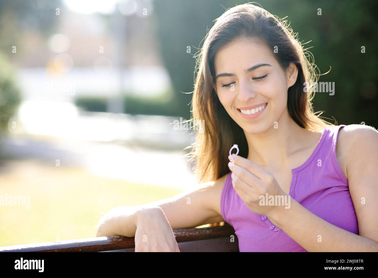 Una donna felice guarda l'anello di fidanzamento seduto in un giardino Foto Stock