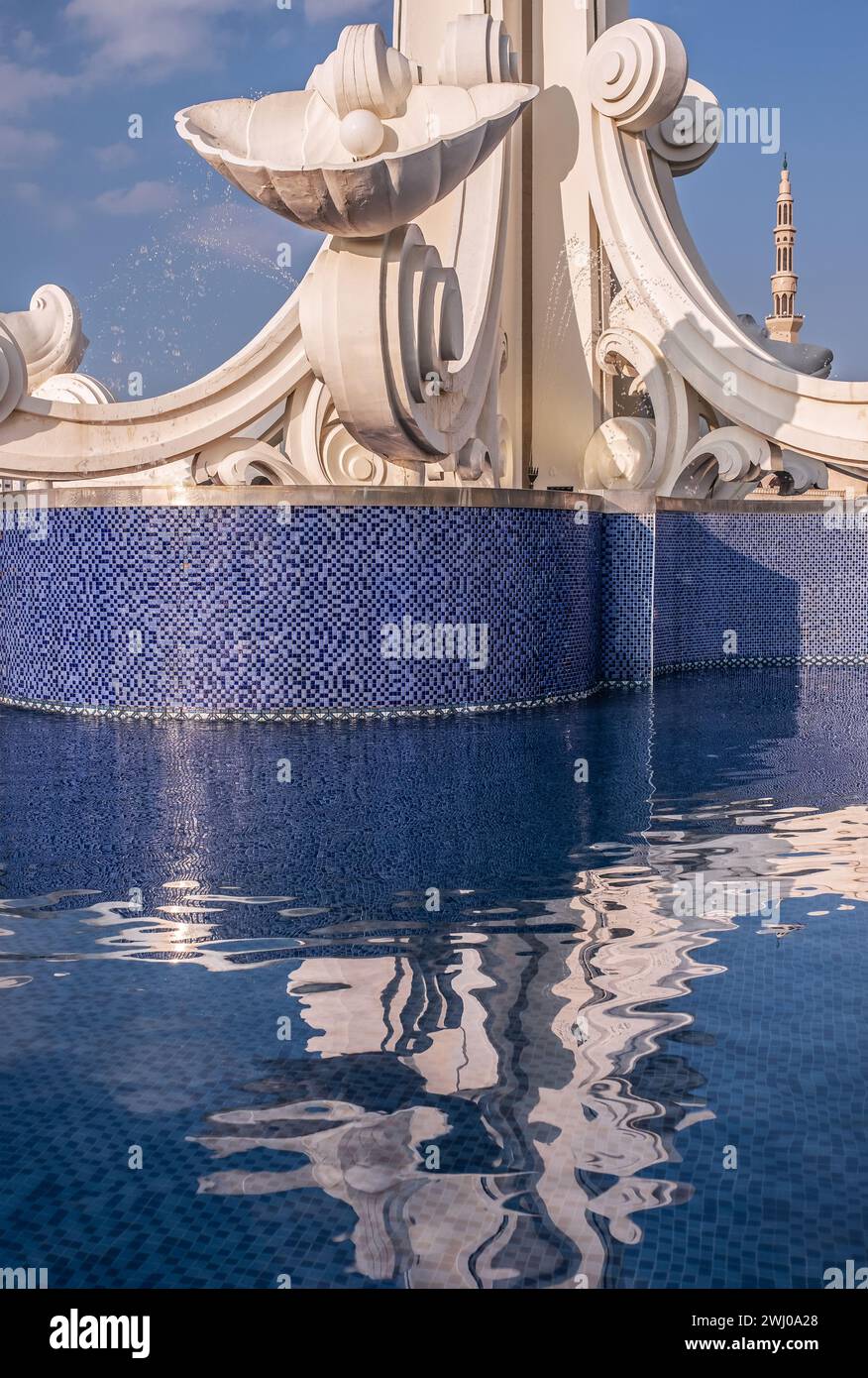 Spettacolare e intricata riflessione sulla superficie dell'acqua nella fontana della città; il minareto della moschea adiacente al parco sullo sfondo Foto Stock